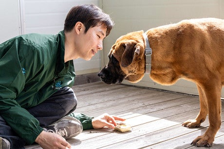 A man sitting on the floor, leaning over greeting a dog