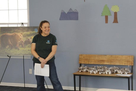 A woman in a Humane World for Animals shirt stands at the front of a classroom, giving a presentation on wildlife conservation to first graders.