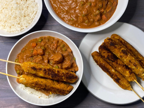 A bowl of White Bean Tikka Masala with skewers and sides.