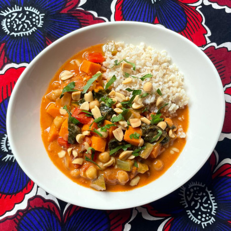 A bowl of West African peanut and chickpea stew in a white bowl on a colorful tablecloth.