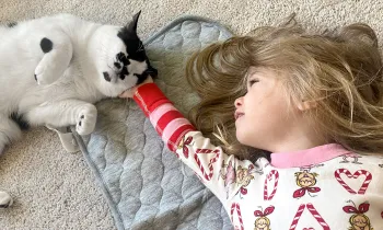 A young girl laying on the floor caresses her pet cat who contentedly leans into her hand