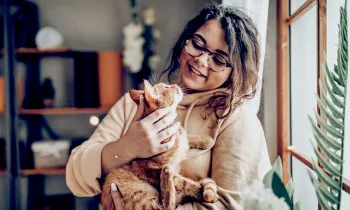 A woman holds a cat in her arms as they look lovingly at each other