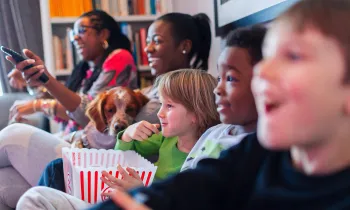 Multi-ethnic family watching movie and eating popcorn on the couch watching a movie with a dog.