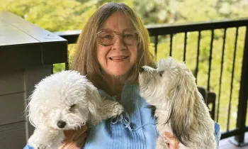 Woman sitting on a deck holding her two white dogs.