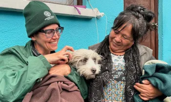 Two women sit outside a vet clinic, holding a dog.