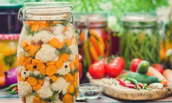 A table full of vegetables on a wooden cutting board and sealed in jars for pickling.