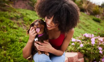 Smiling young woman sitting with her cute little dachshund outside