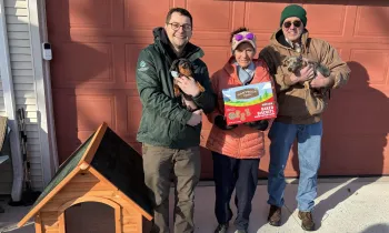 a group of people standing next to a doghouse, holding dogs and treats