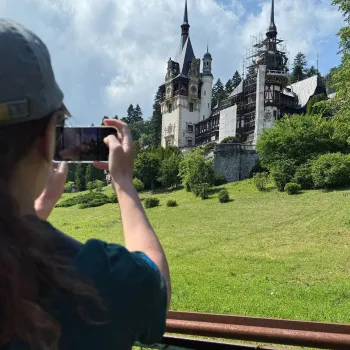 Over the shoulder perspective of a person using their phone to take a picture of a large castle in the distance.