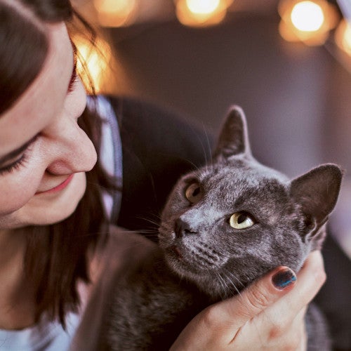 A woman cuddles with her cat who is looking at her adoringly.