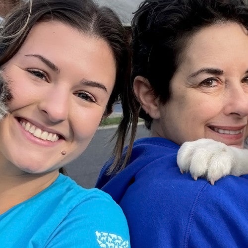 Two women are holding puppies and smiling at the camera