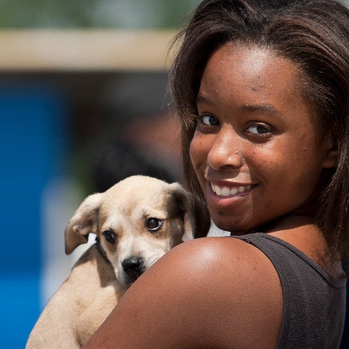 Young woman holds on to dog in line for clinic giving out shots and food