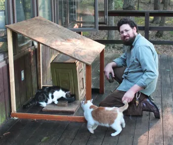 Jim O'Hagan sitting with colony cats at feeding station