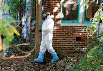 Rescuer in protective gear approaching the exterior of the house where an alleged neglect situation is taking place.