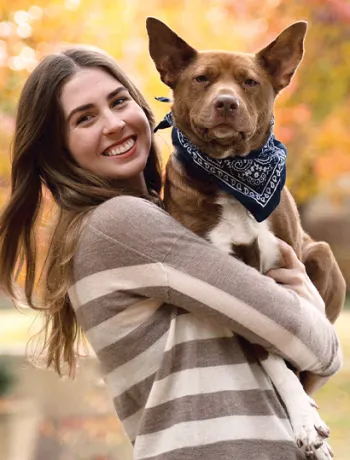 A woman holding a brown dog outside