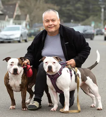 A man kneeling next to two dogs outside.