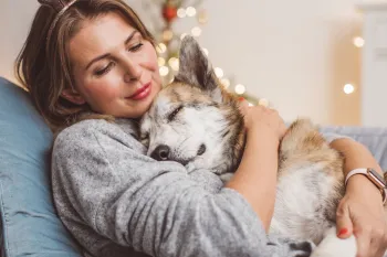 Woman and her dog cuddling on the couch with holiday lights behind them