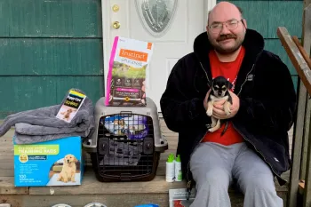 Man sitting with his new puppy sitting on his porch filled with pet supplies
