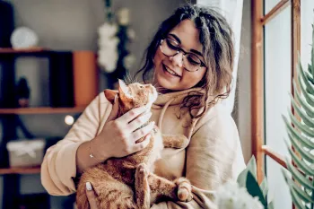 A woman holds a cat in her arms as they look lovingly at each other
