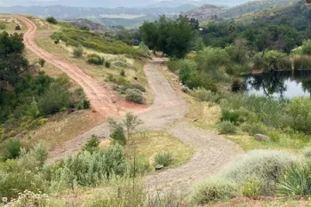 A dirt and gravel road on a hillside with water and low mountains in the background