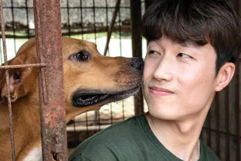 Sangkyung Lee, Dog Meat Campaign Manager of HSI Korea, interacts with a dog at a dog meat farm
