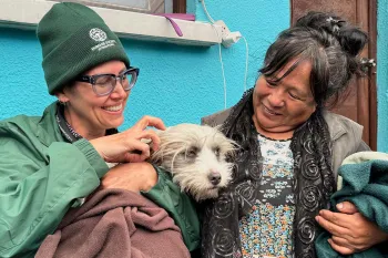Two women sit outside a vet clinic, holding a dog.