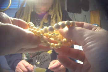 The image shows a person holding a string of ivory beads in their hands. 