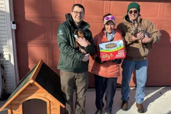 a group of people standing next to a doghouse, holding dogs and treats