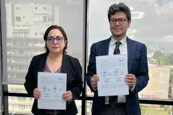 Two people standing, each holding a signed document.