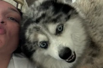person is taking a close-up selfie on a couch with a fluffy dog