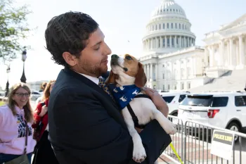 A person holding a small dog outside the United States Capitol building.