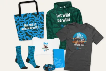 Collection of Humane World for Animals branded merchandise, including a shirt, hooded sweatshirt, socks, notebook, dog collar, tote bag and pet placemat that can be bought to support animals