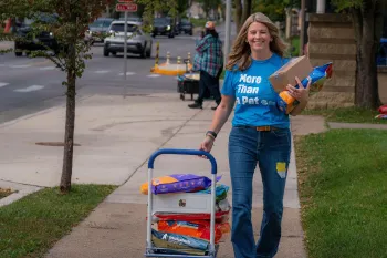  Smiling woman walking, pulling a small cart loaded with large bags of pet food.