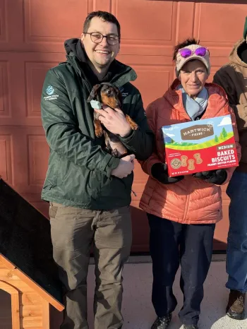 a group of people standing next to a doghouse, holding dogs and treats
