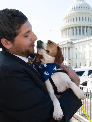 A person holding a small dog outside the United States Capitol building.