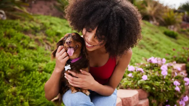 Smiling young woman sitting with her cute little dachshund outside