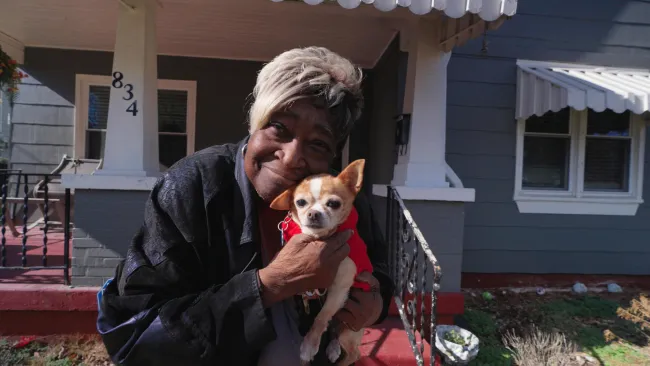 woman stands in front of house holding a dog close to her face