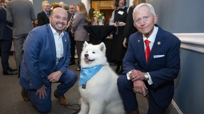 two men kneeling down to take a photo with a dog