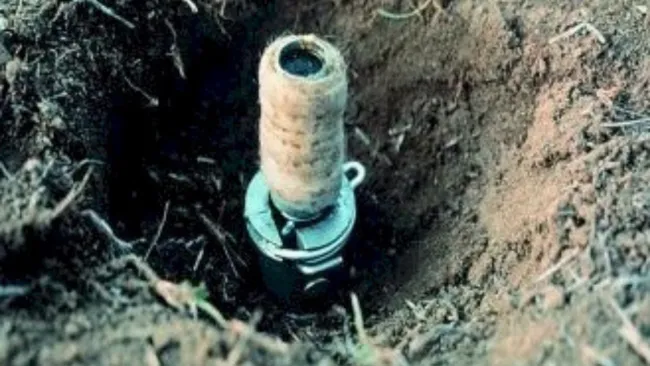 A small metal device partially embedded in a shallow hole in the ground