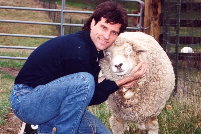 A man snuggling a sheep.