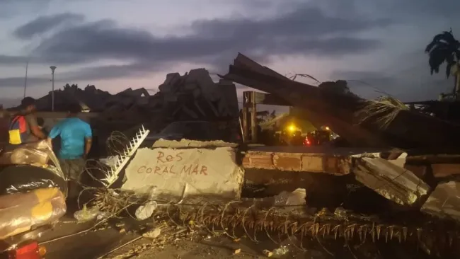 A scene of heavy destruction with large slabs of concrete and twisted rebar scattered across the ground.