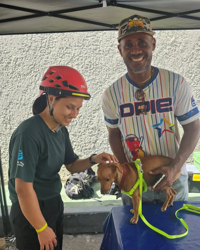 Two people are standing with a small brown dog