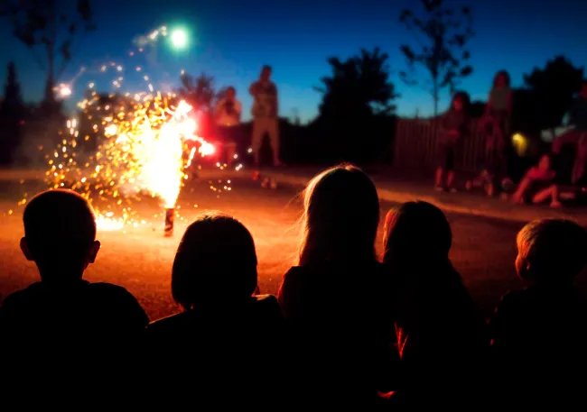 Children watching fireworks at an outdoor nighttime gathering.