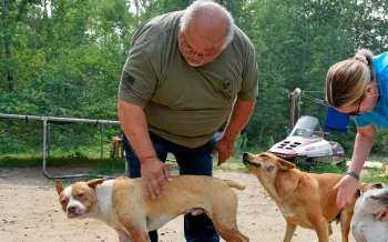 Rick Haaland of Leech Lake Band of Ojibwe Pets for Life and Rachel Thompson from Pets for Life pet three dogs outside a home