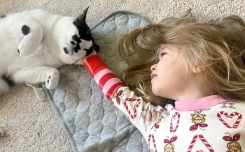 A young girl laying on the floor caresses her pet cat who contentedly leans into her hand