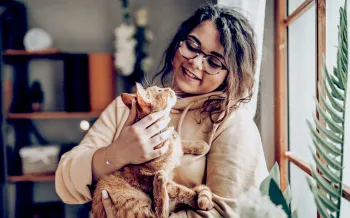 A woman holds a cat in her arms as they look lovingly at each other