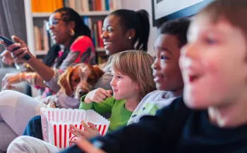 Multi-ethnic family watching movie and eating popcorn on the couch watching a movie with a dog.