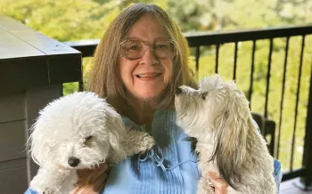 Woman sitting on a deck holding her two white dogs.