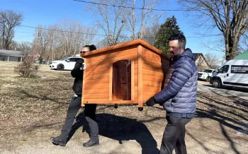 Two people carrying a doghouse