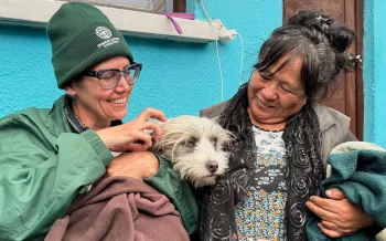 Two women sit outside a vet clinic, holding a dog.